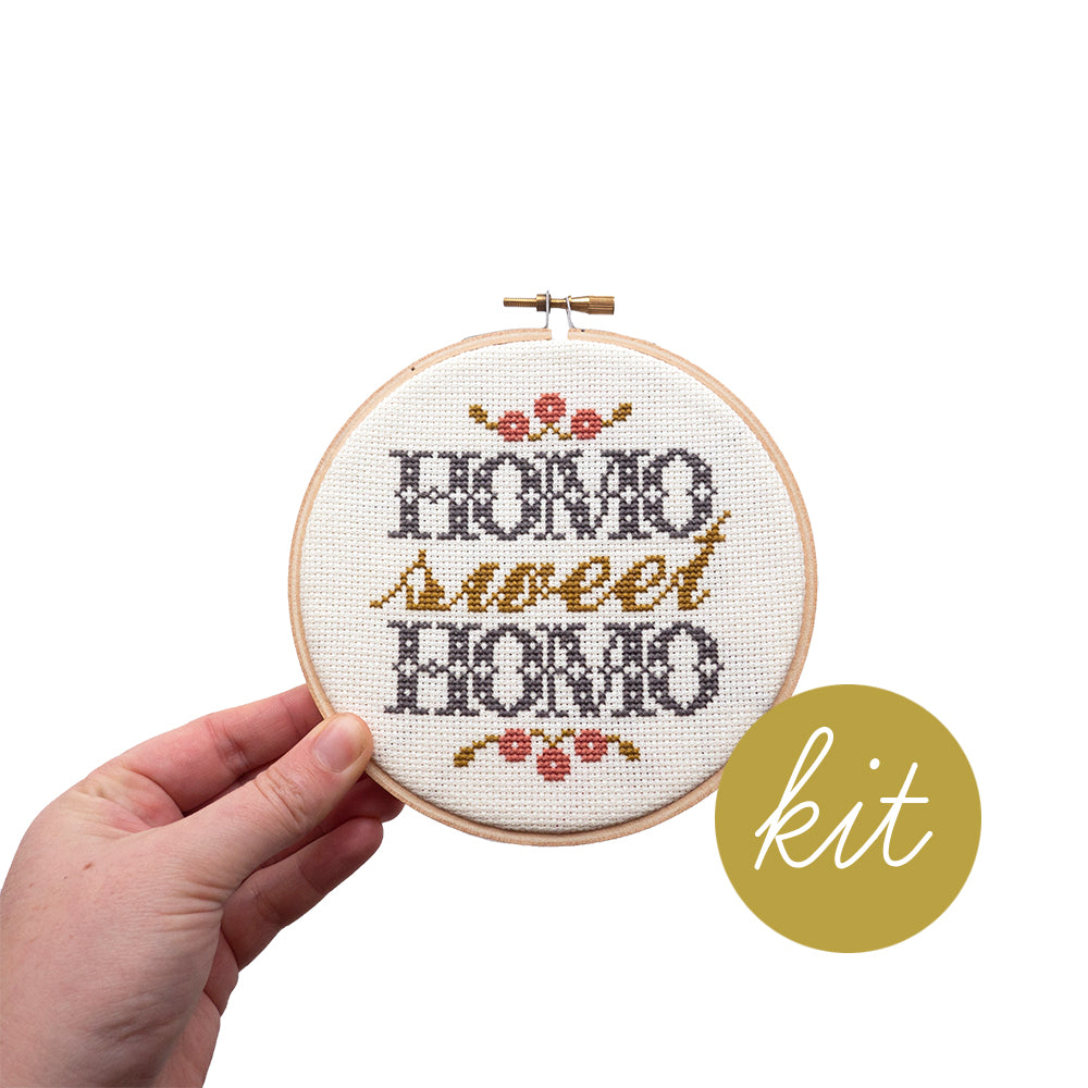 traditional grey and gold text reads Homo Sweet Homo with pink and gold flowers, DIY cross stitch kit